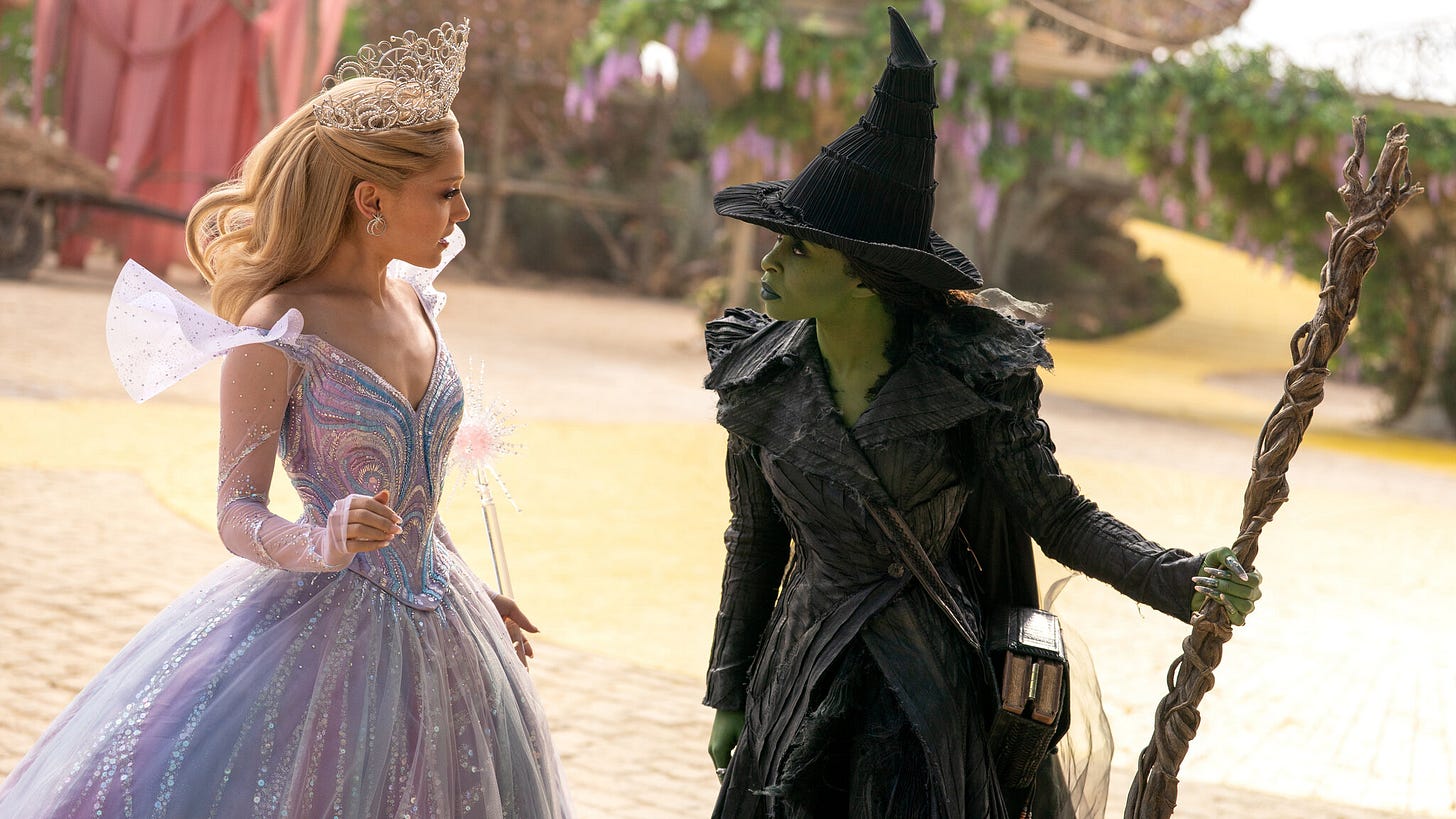 In a still from the film set on the yellow brick road of Oz, the green witch played by Cynthia Erivo is holding her broom and looking angrily at the good witch played by Ariana Grande.