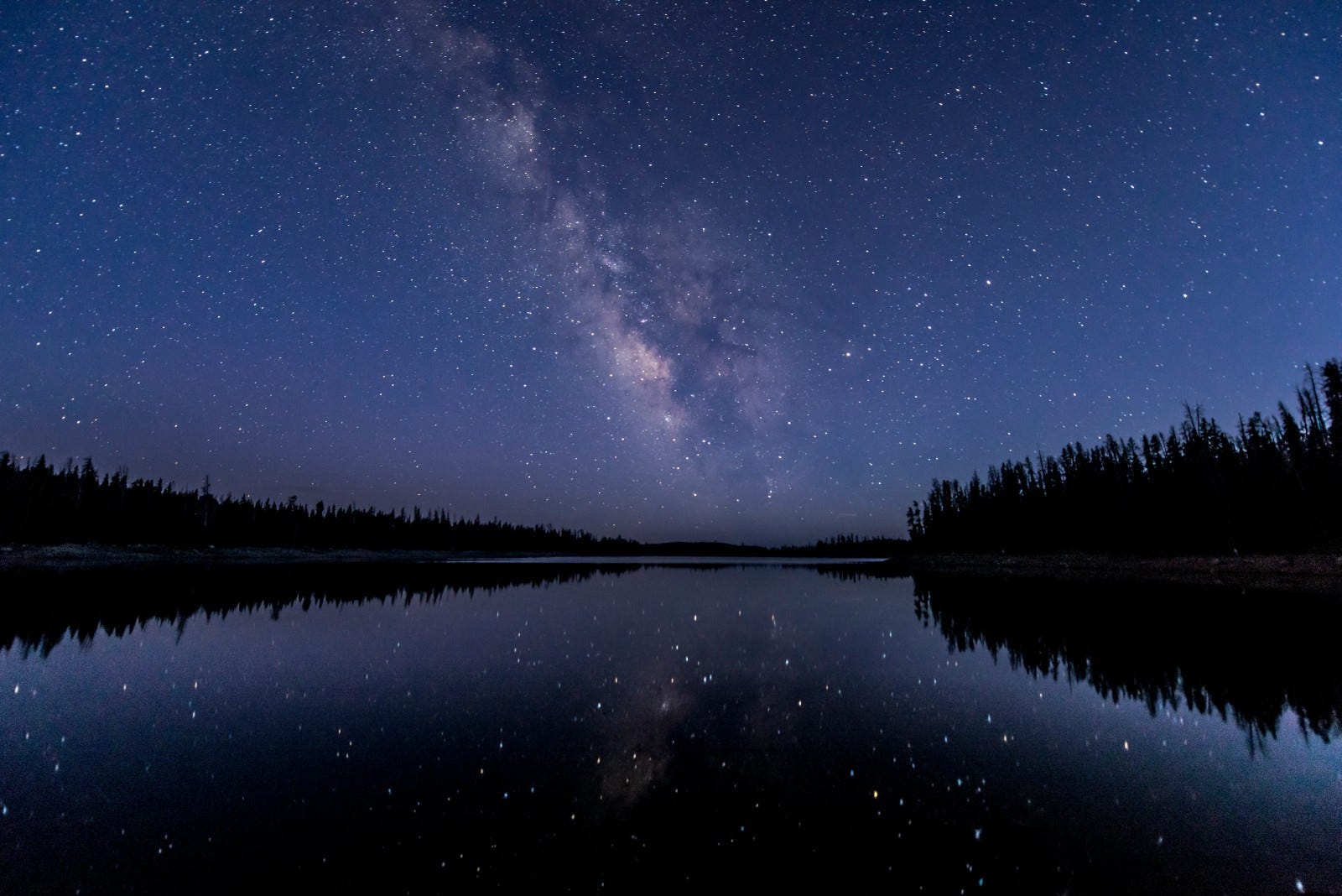 A quiet nighttime horizon with dark water reflecting a bright, star-filled sky. Above and below are one.