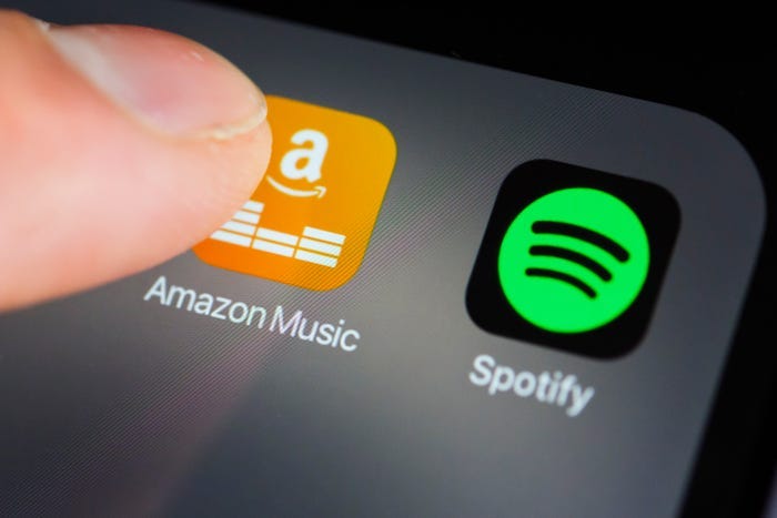 The Amazon Music and Spotify app icons on an iPhone, with a user tapping the Amazon icon.