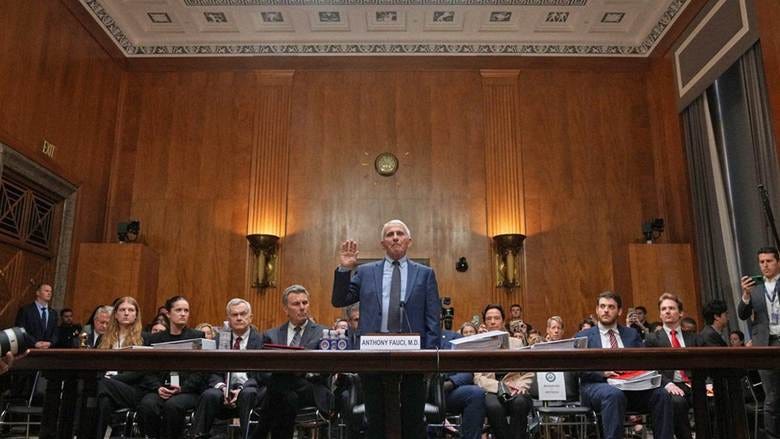 Photograph of Dr. Anthony Fauci standing up in a government hearing with his right hand raised.