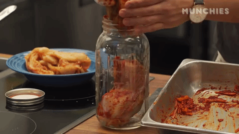A person's hand stuffs red-coated cabbage leaves into a jar. A person's hand stuffs red-coated cabbage leaves into a jar.