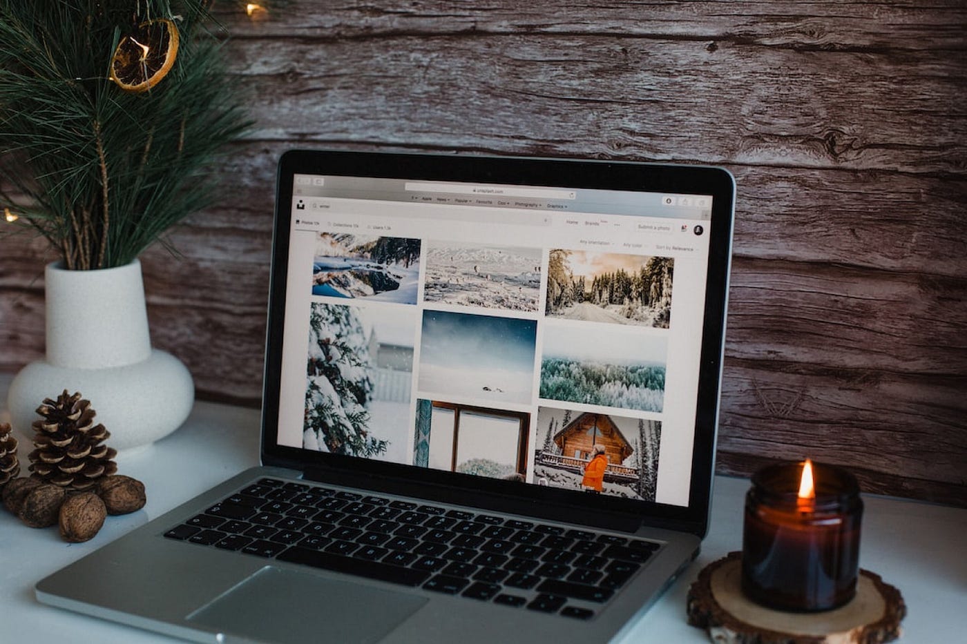 The image shows a laptop on a desk surrounded by winter and Christmas ornaments such as a candle and pine combs.