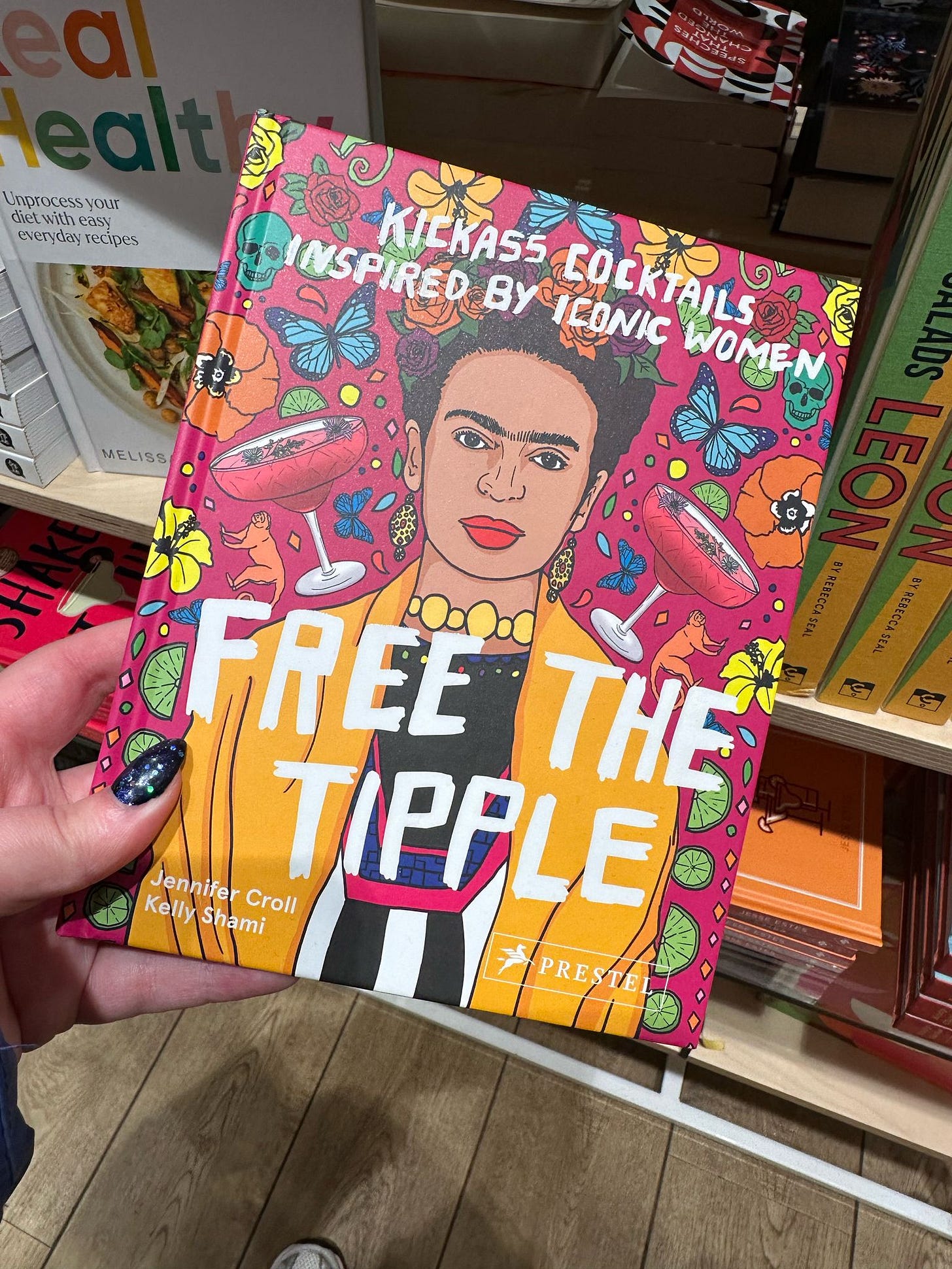 a hand holding a book called Free the Tipple, which features Frida Kahlo on the front