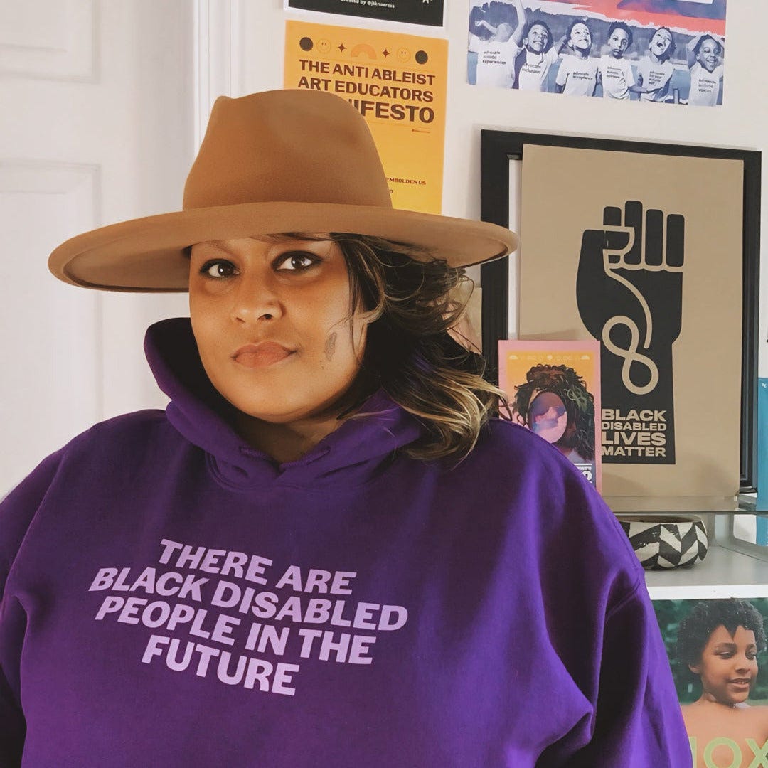 Person wearing a purple hoodie with text, standing in front of a wall with various posters.