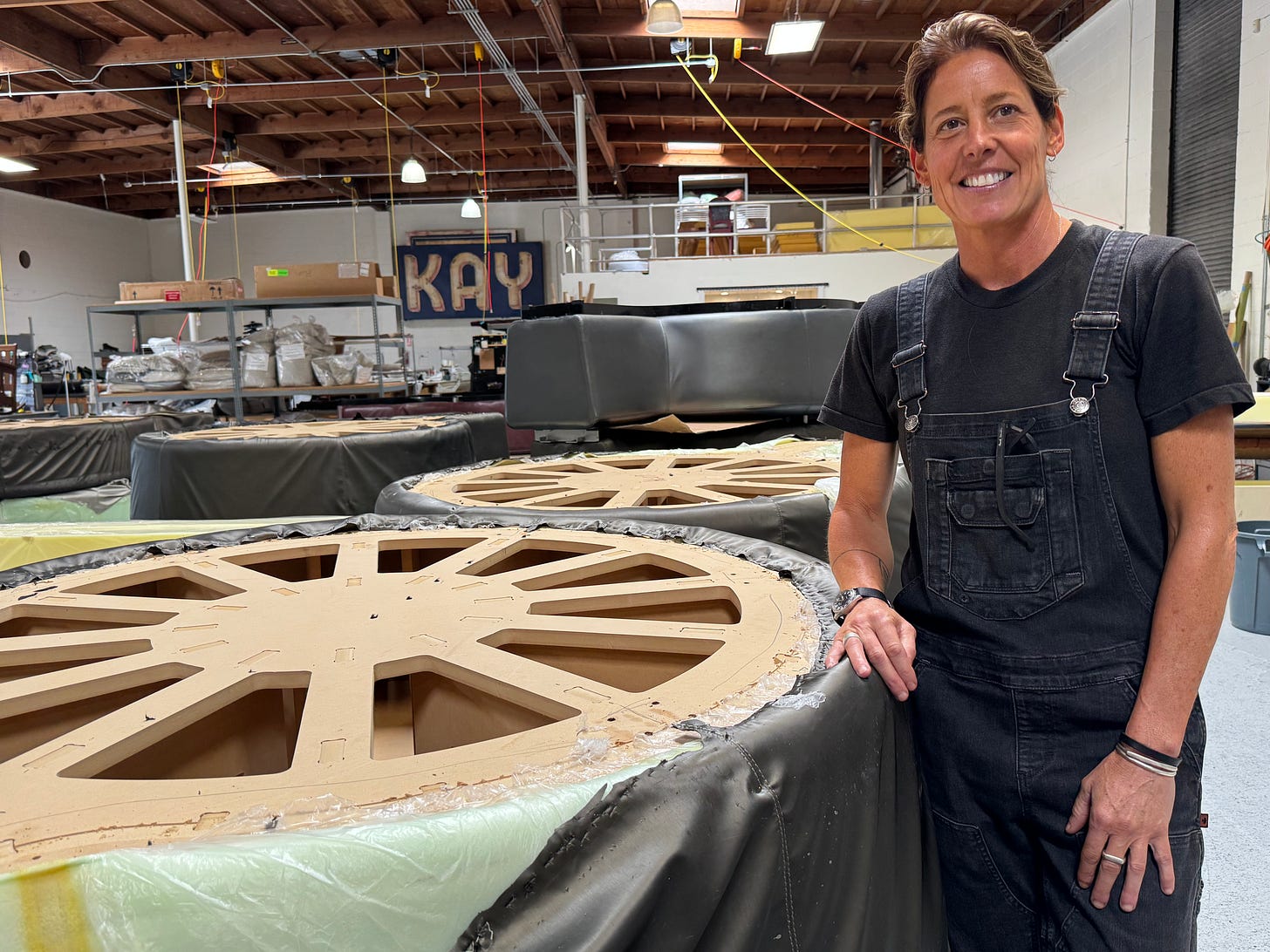 Cindy Feinauer, an upholsterer, stands in her workshop surrounded by large circular furniture frames and upholstery materials.