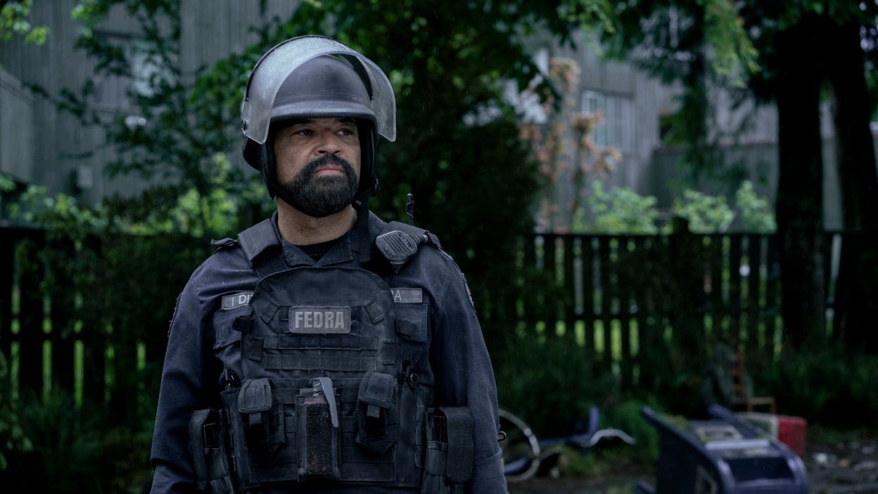 A man stands outside wearing a dark soldier's uniform with a logo reading "FEDRA."