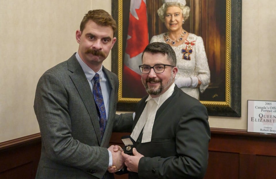 Two men shaking hands in front of a portrait of Queen Elizabeth II.