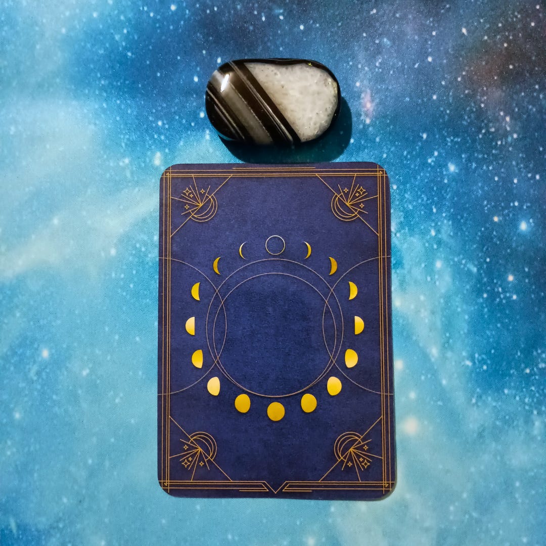New Moon Magic: Your August 2025 Pick-a-Card Tarot Reading, pile 4 — black agate stone and an oracle, face down on a starry blue background