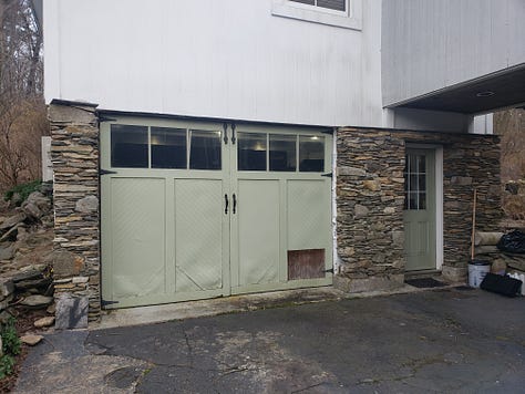 A green car garage door. An grow tent with empty racks. An empty garage with boxes and things.