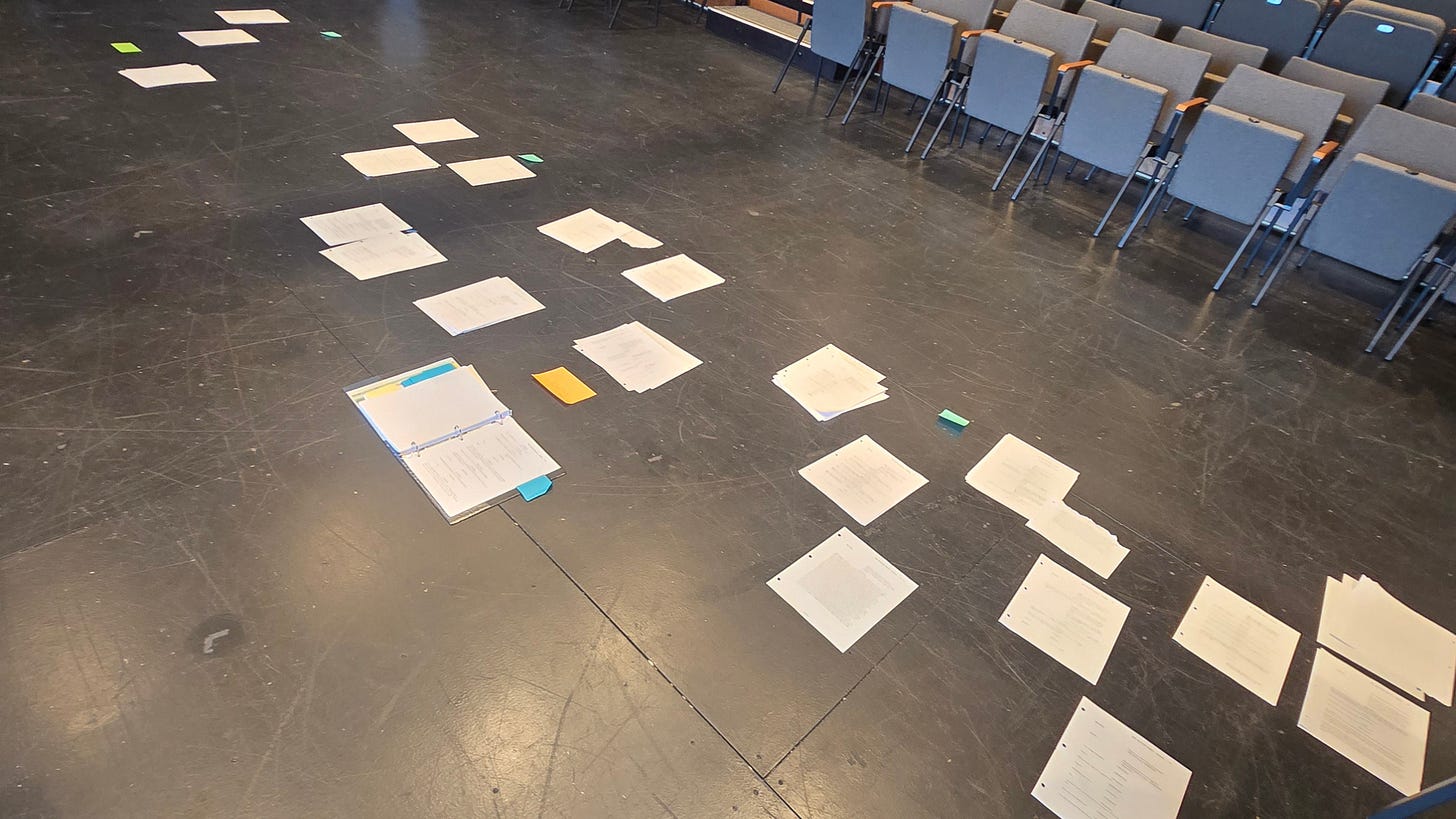 Printed pages from The Quilted Heart are laid out across the rehearsal room floor, allowing the creative team to study the play's structure, rearrange scenes, and identify patterns that weren't visible on the page alone.