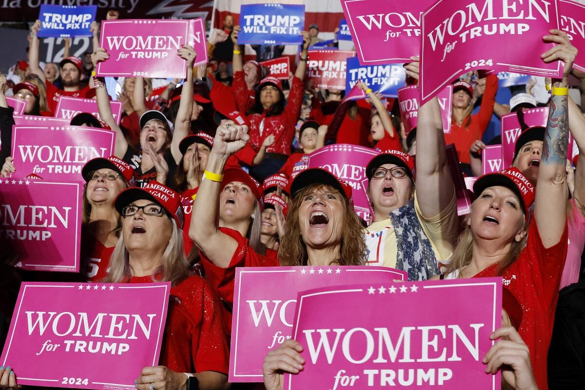 A group of white women cheering at a Trump rally holding signs that say "Women for Trump"