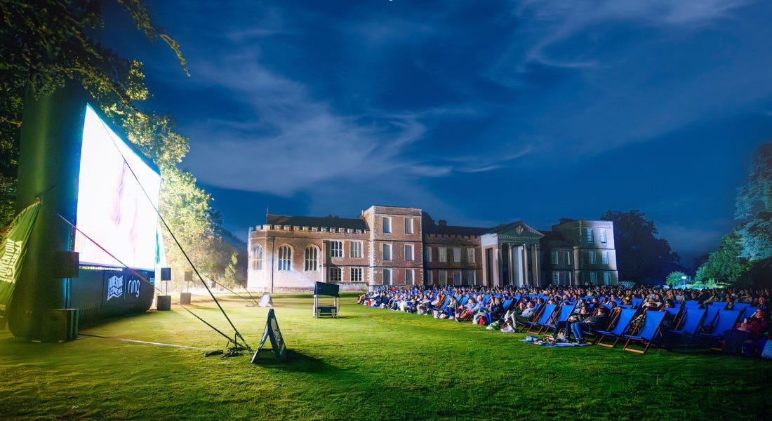 An outdoor cinema screen at night with a large screen to the left and blue deckchairs to the right