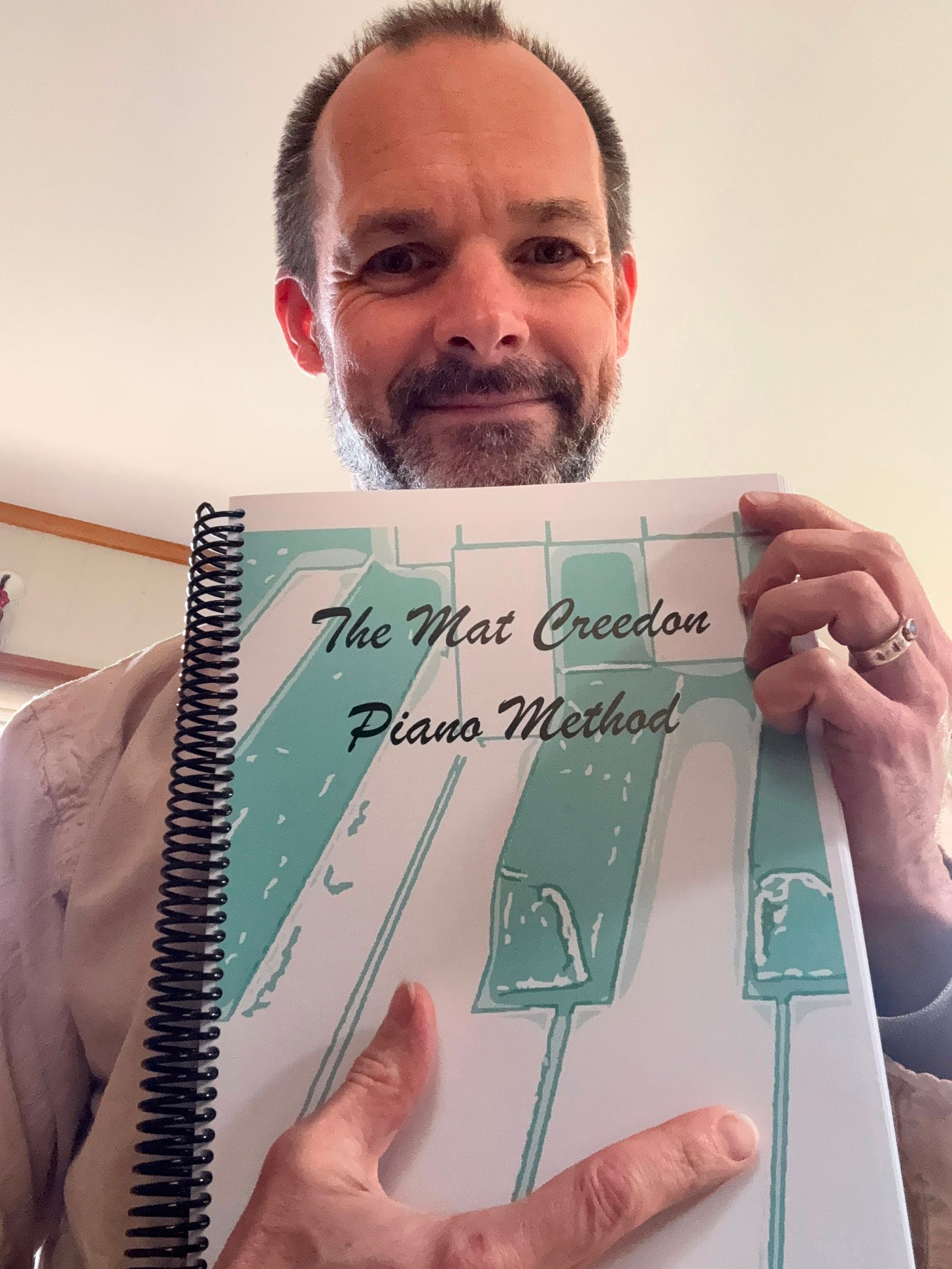 Mat Creedon holding a printed copy of The Mat Creedon Easy Key Method, a music education book developed over many years of teaching and performance.