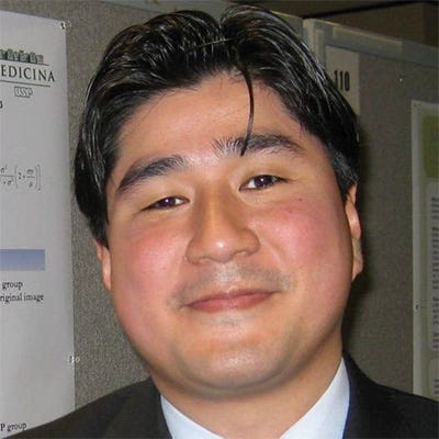 A imagem contém homem com cabelo preto curto penteado para trás e um sorriso. Ele veste paletó preto, camisa branca e gravata. A imagem contém homem com cabelo preto curto penteado para trás e um sorriso. Ele veste paletó preto, camisa branca e gravata.