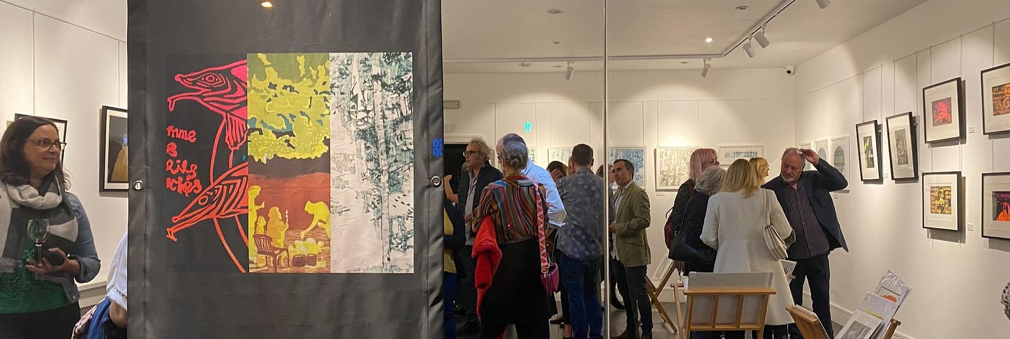 Image of large banner hanging in the window promoting the exhibition that is taking place behind it. Various visitors are talking and looking at the framed art on walls.