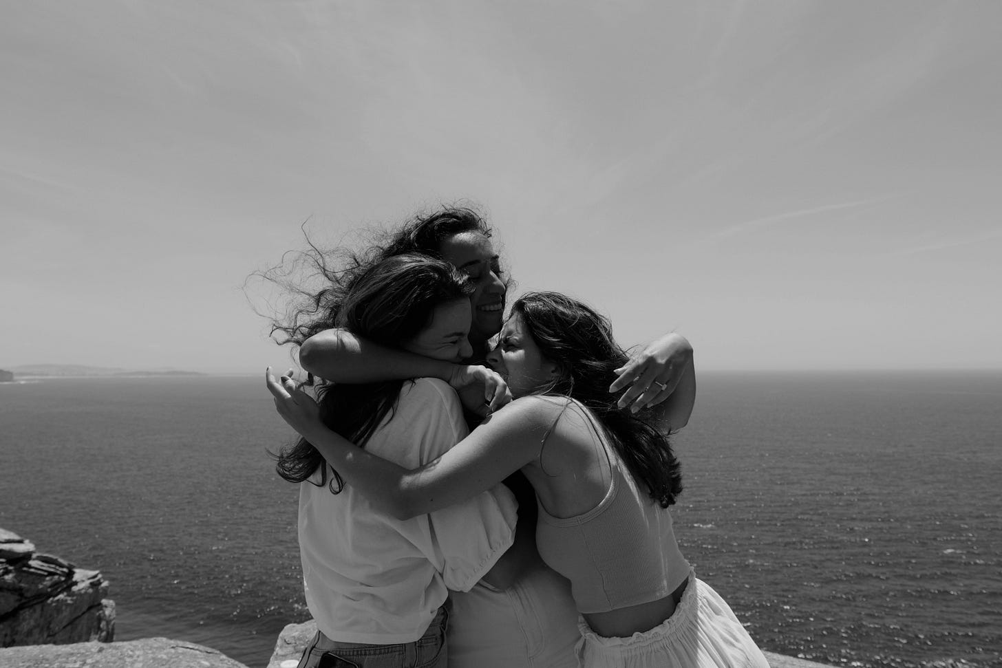 A black and white photo of three friends hugging by the ocean.