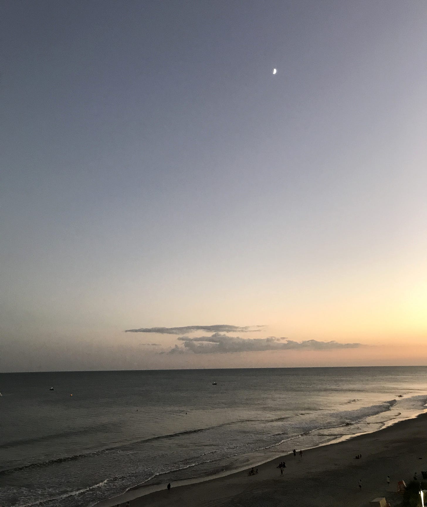 A crescent moon in a fading blue sky above the ocean at dusk, with soft waves and small figures walking along the beach. A crescent moon in a fading blue sky above the ocean at dusk, with soft waves and small figures walking along the beach.