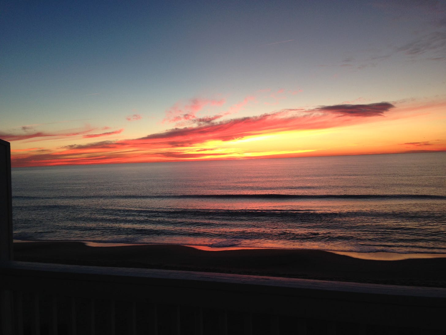 A peachy golden sunrise over a dark, calm ocean.
