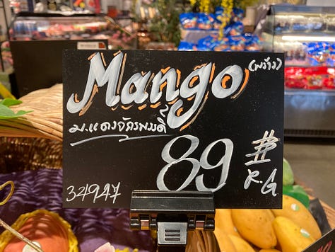 Signs and displays of unusual mango varieties at a grocery store in northern Thailand, including Megumi and Tsuya mangos.