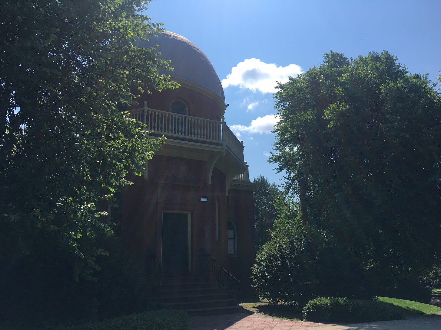 A domed brick building surrounded by trees on a sunny day
