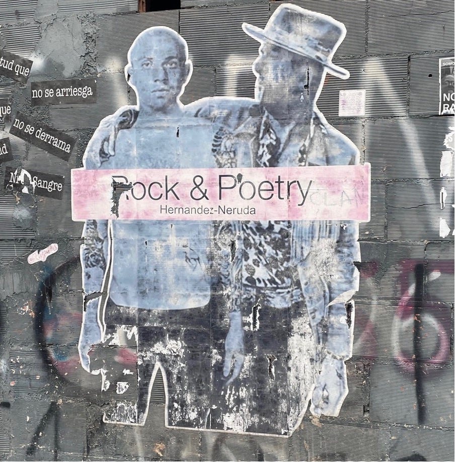A photo of graffiti on a stone wall. There are two men in the middle of the image. The text reads: 'Rock & Poetry. Hernandez-Neruda.'