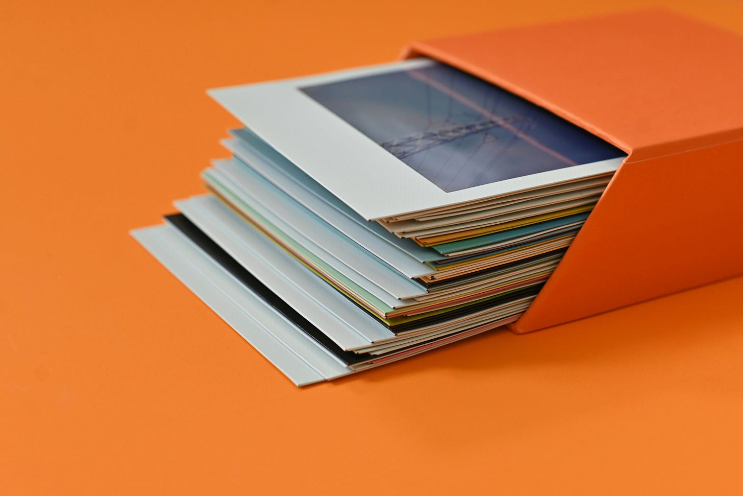 A stack of polaroids peeking out of an orange box on an orange background