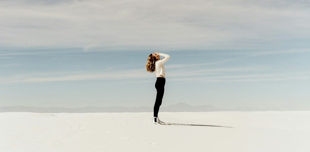 woman looking up to the sky while standing on white sand