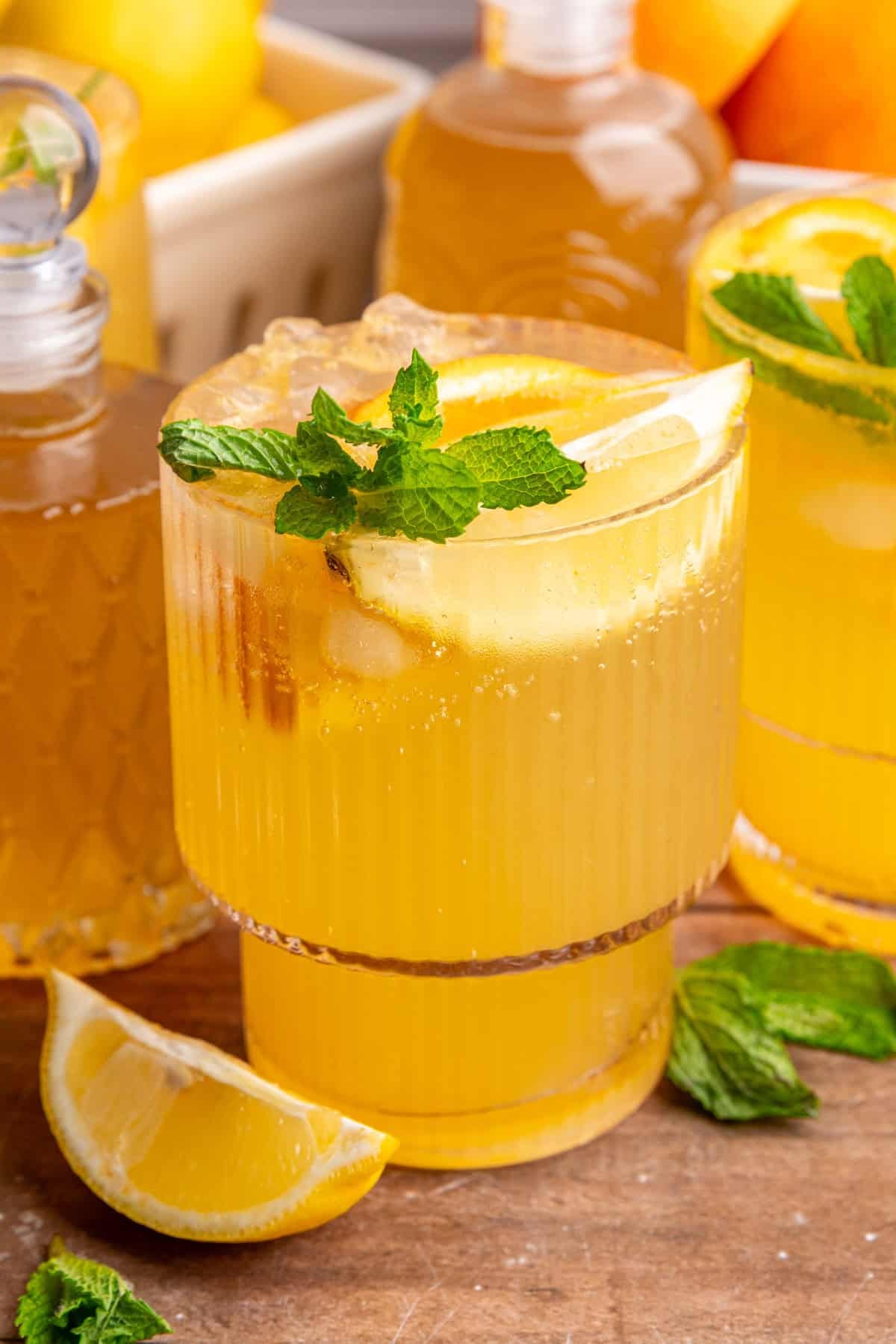 A few glasses of citrus mocktail on a table with jars of lemon ginger syrup.