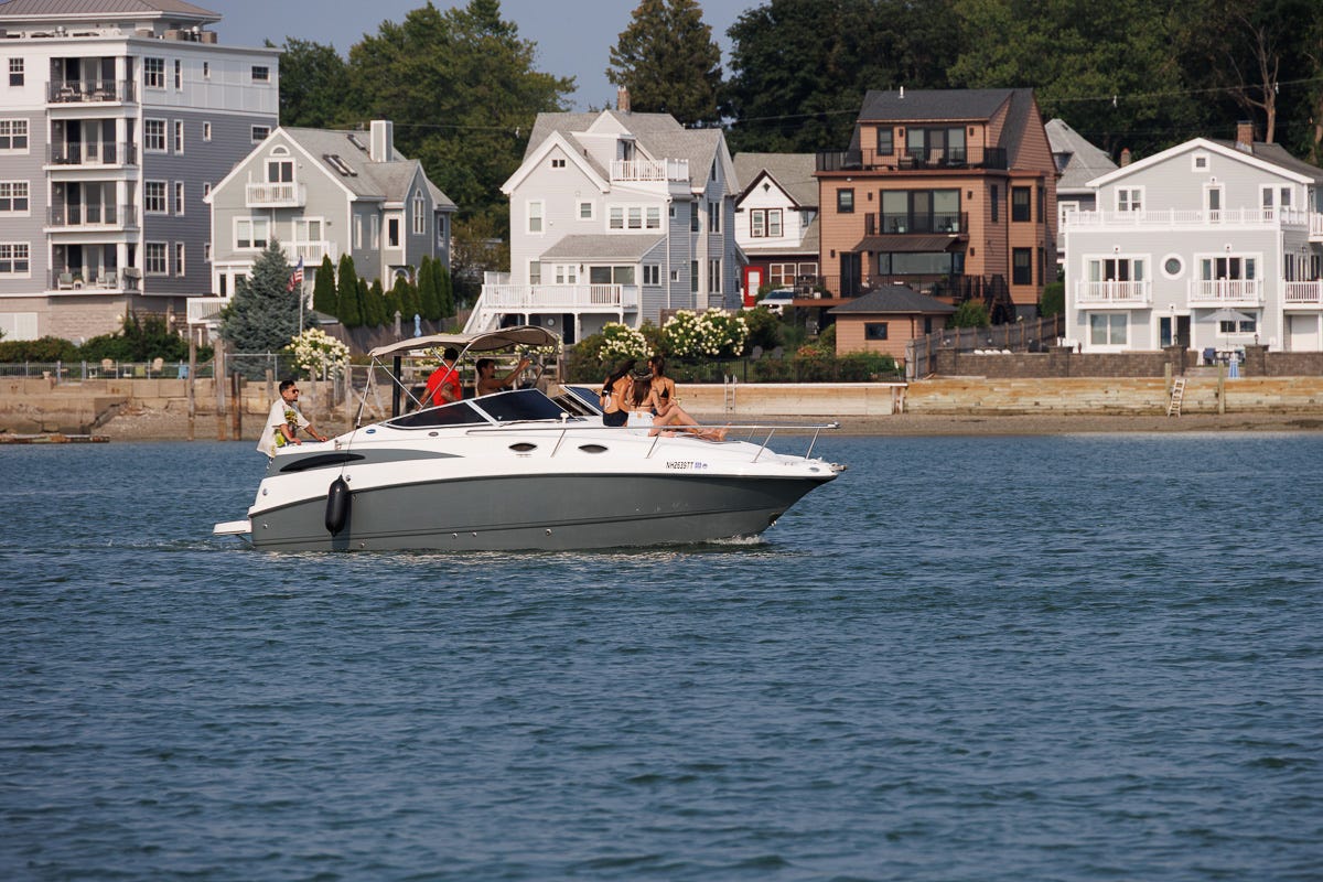 Gray and white motorboat with people onboard passing houses along the Boston waterfront