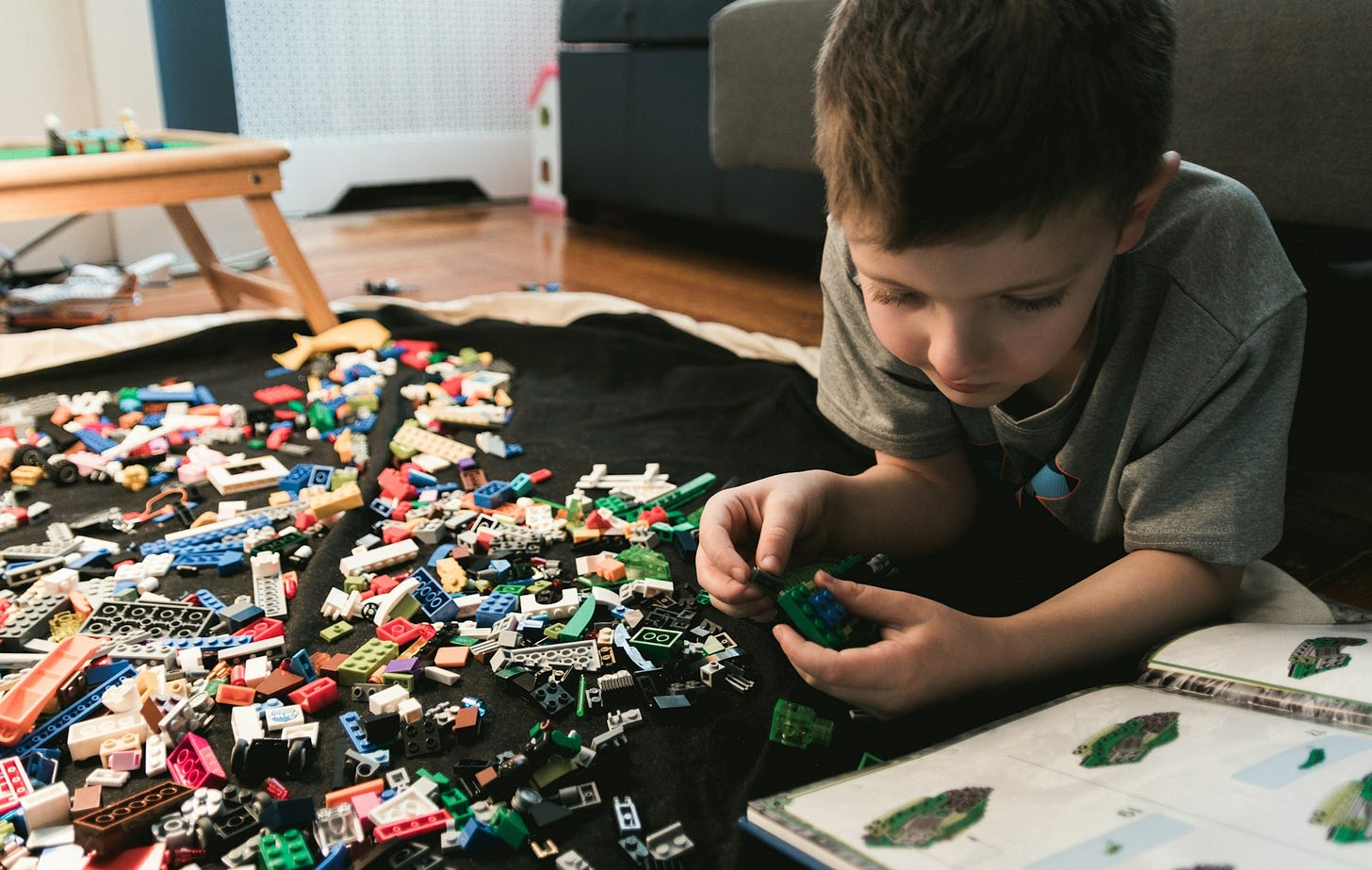 A young boy lying on a living room carpet playing lego and looking at a lego book. A young boy lying on a living room carpet playing lego and looking at a lego book.