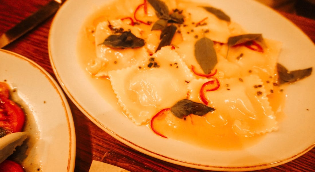 A plate of ravioli with basil and chilli on top A plate of ravioli with basil and chilli on top