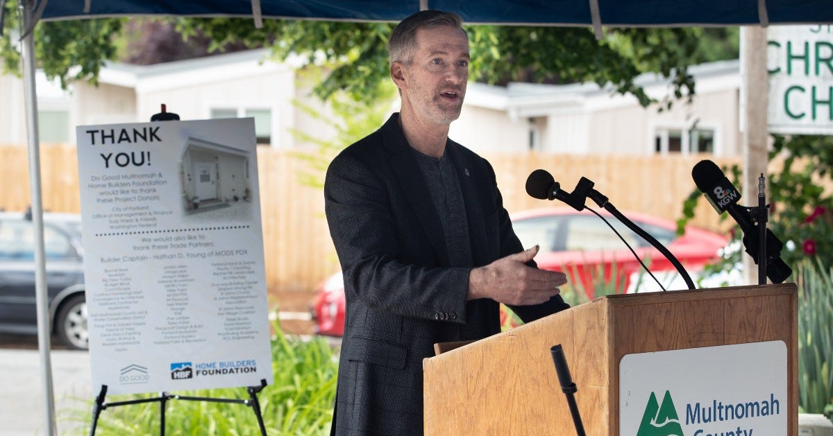 Mayor Ted Wheeler talks at a podium with the Multnomah County logo.