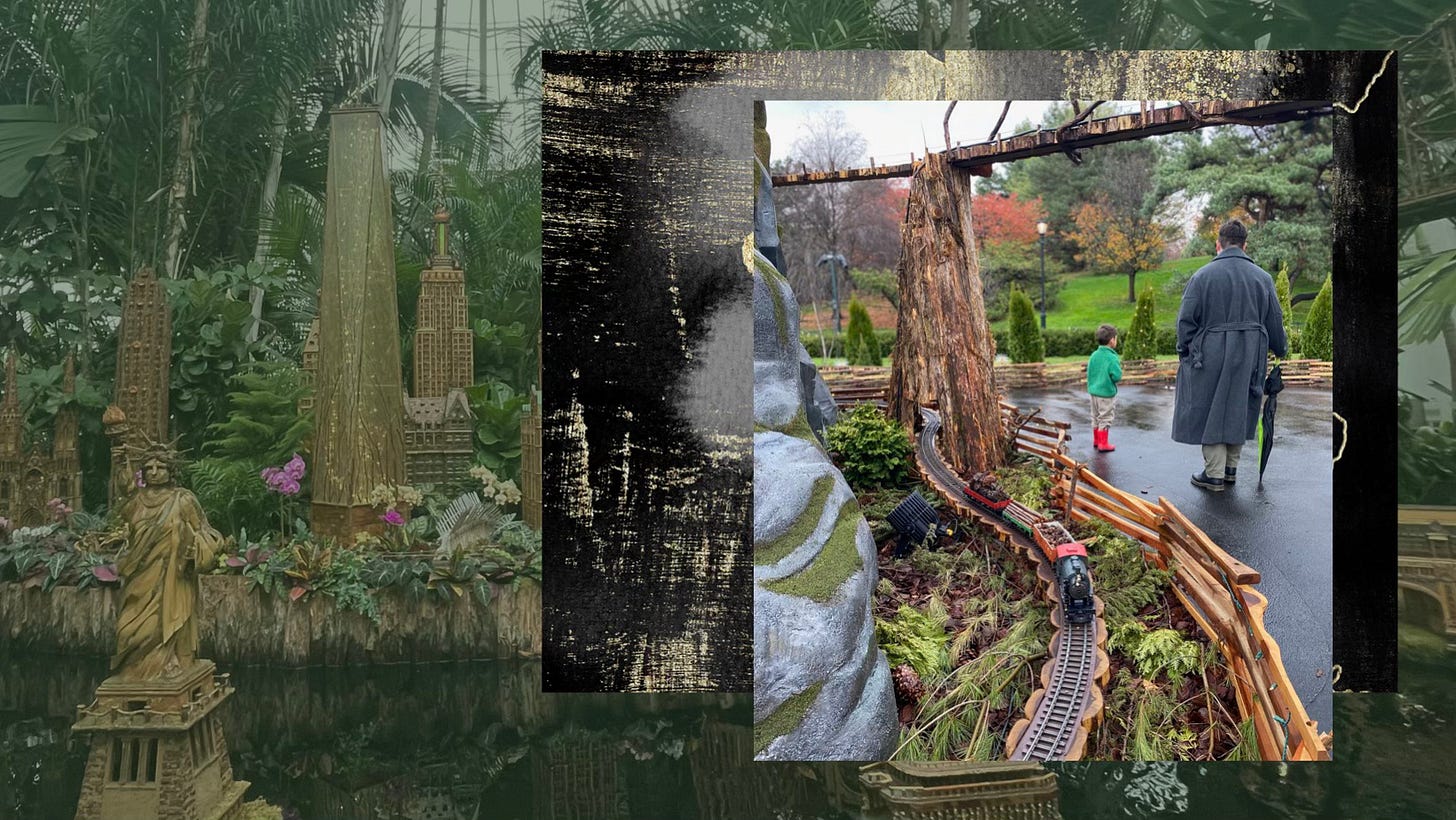 Emrhys, a white masc of center person is wearing a large gray coat and jeans while he walks away from the camera next to their child, CB. CB is also walking away in a green fleece, to the left of them both is a model train from the New York Botanical Garden. This image is laid over a black, gold and gray abstract slab of paint. Behind both of these images, there's a faded greenish hued picture of the New York Botanical Garden's rebuild of the Statue of Liberty and other New York landmarks rebuilt and modeled from natural materials.