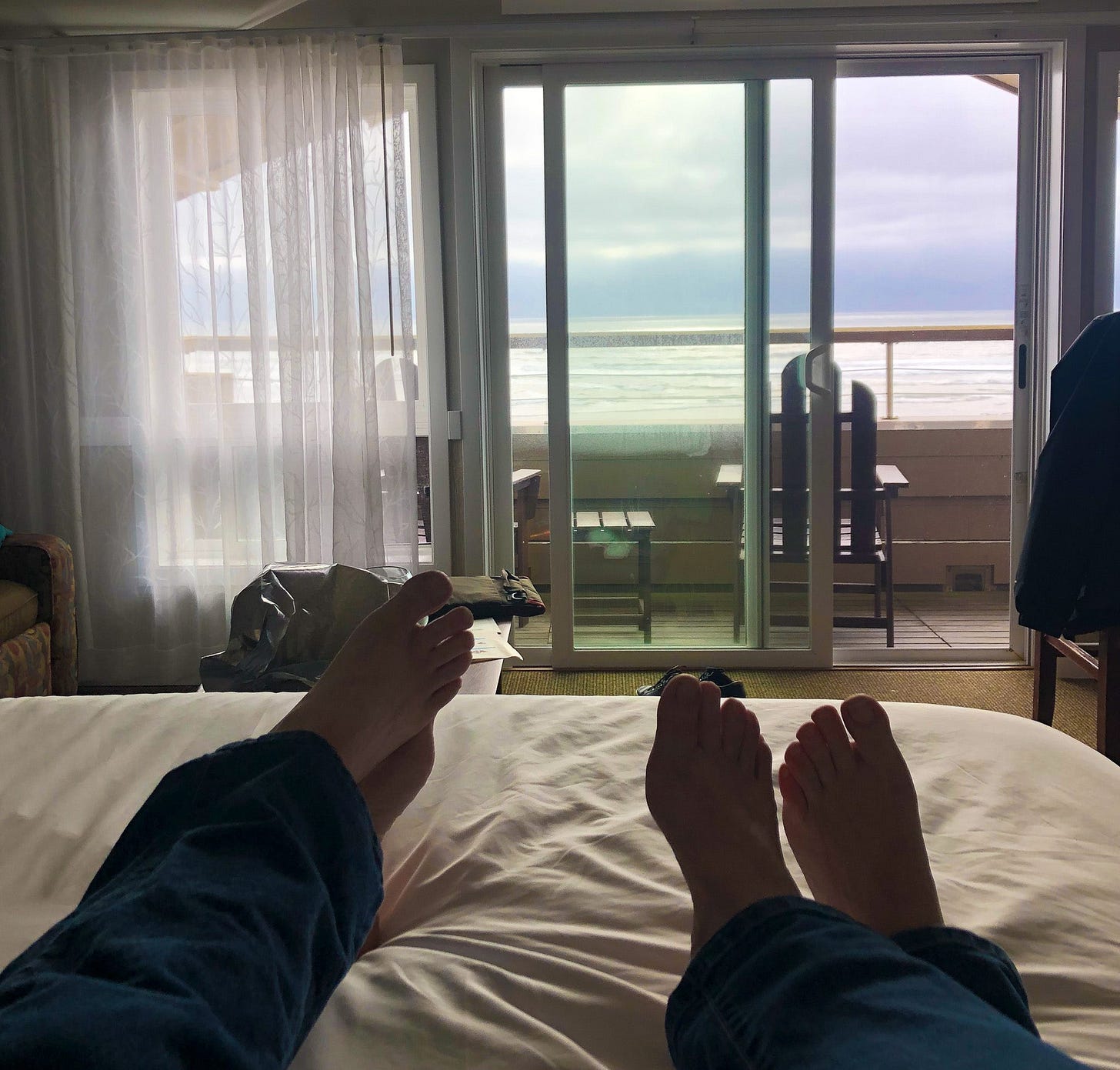 silhouette of feet on a hotel bed looking out a sliding glass door