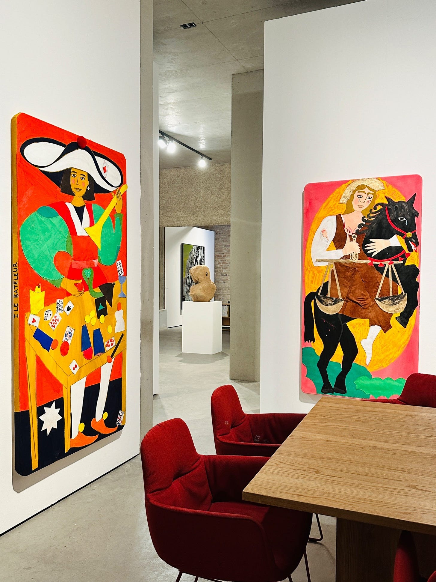 Colorful figurative painting by Johanna Dumet installed in a gallery dining area, showing a stylized woman in bold red, yellow, green, and black tones.