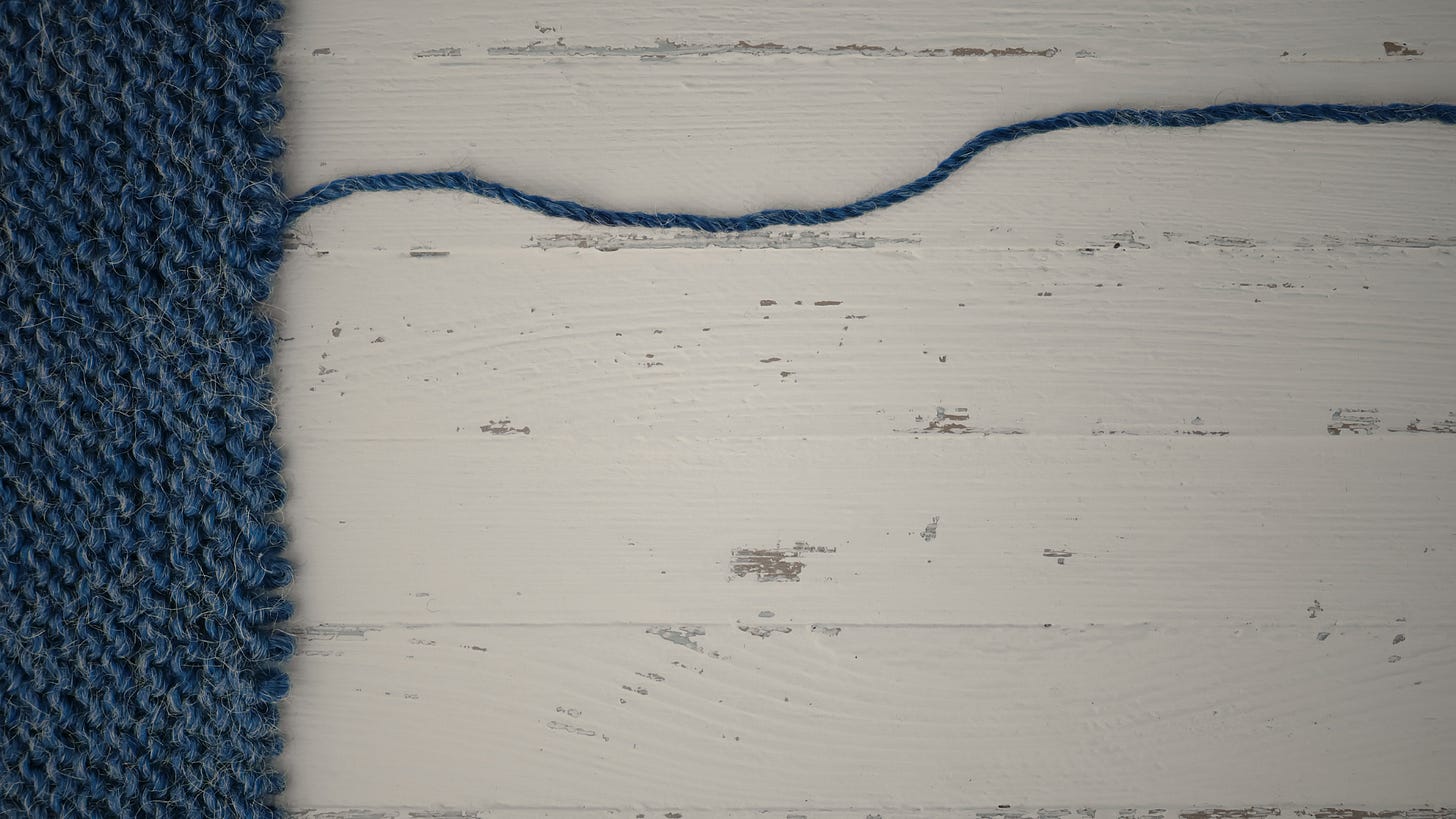 Blue yarn on a white, fading wooden background, a single string extended across the top of the frame threatening to unravel the woven material. Blue yarn on a white, fading wooden background, a single string extended across the top of the frame threatening to unravel the woven material.