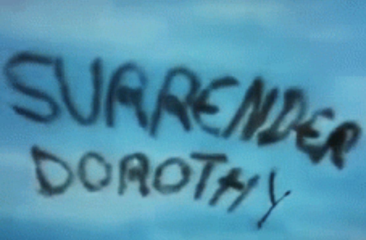 Film still from Wizard of Oz - a witch writers "Surrender Dorothy" across the sky with her broom.