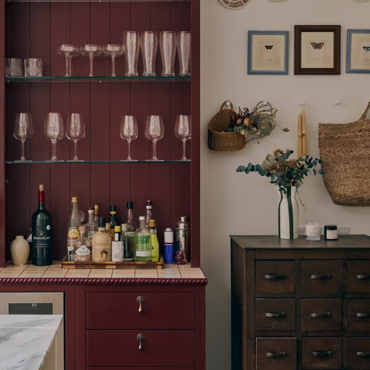 This may contain: there are many bottles and glasses on the counter in this room with red cabinetry