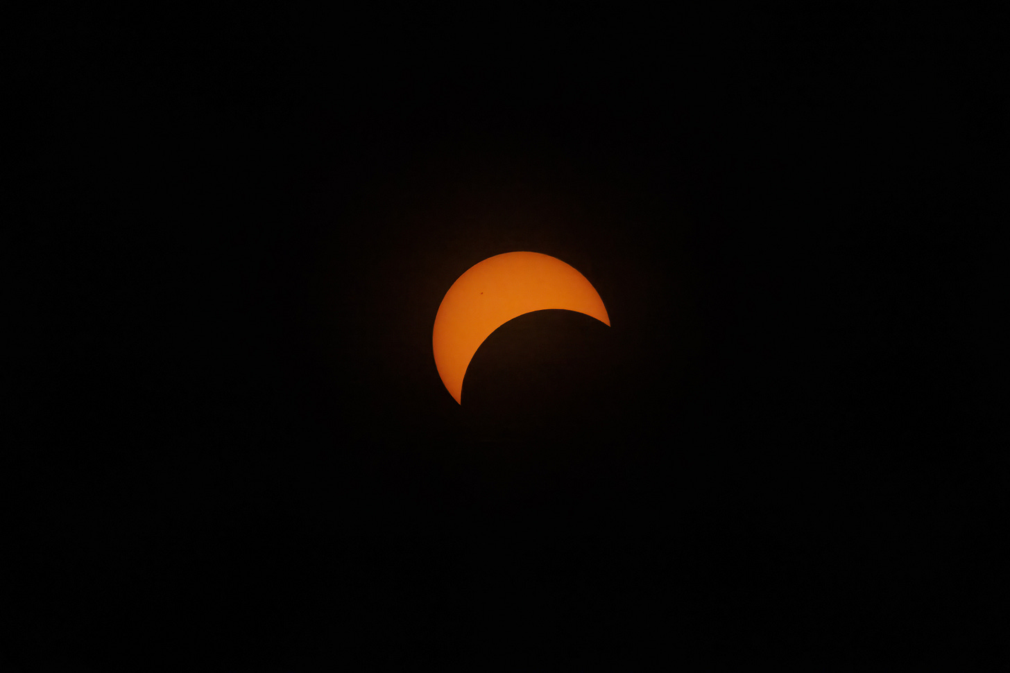 The moon partially obscuring the sun, making it look like a red-orange crescent.