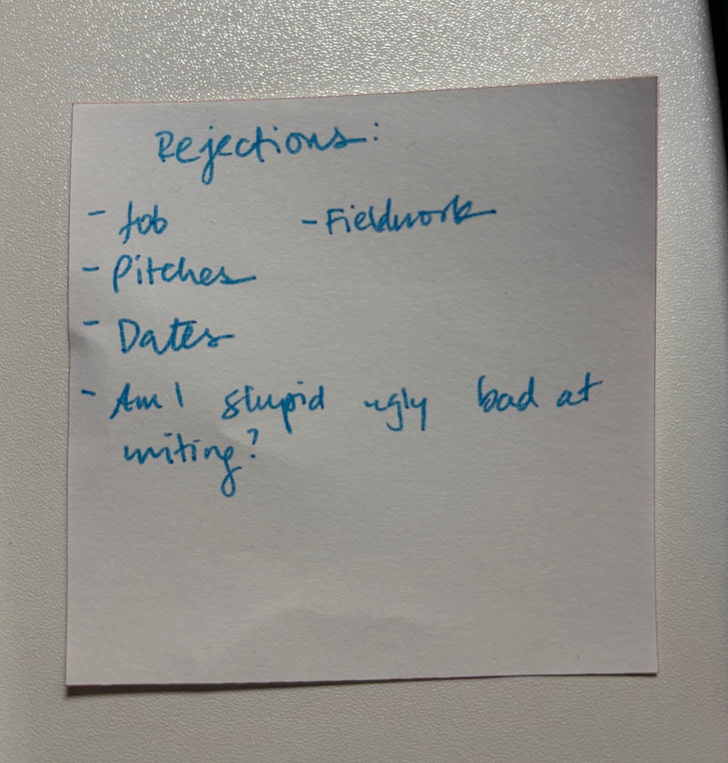 White sticky note with blue handwritten text that says "Rejections: Job, fieldwork, pitches, dates, am I stupid ugly bad at writing?