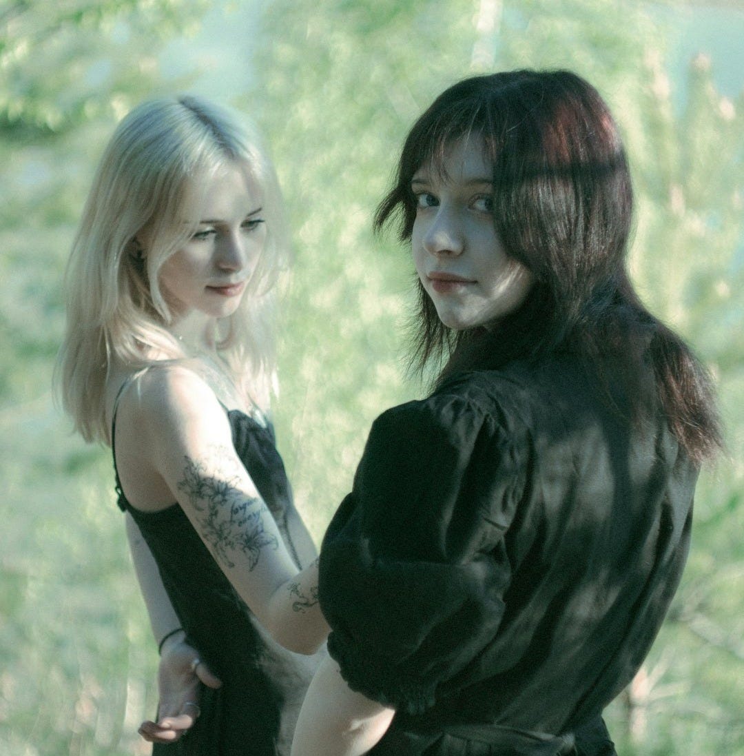 Two young women in black dresses outdoors.