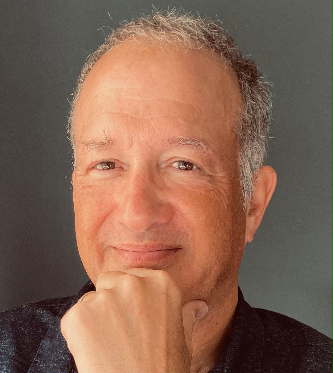 A man touches his chin and smiles at the camera
