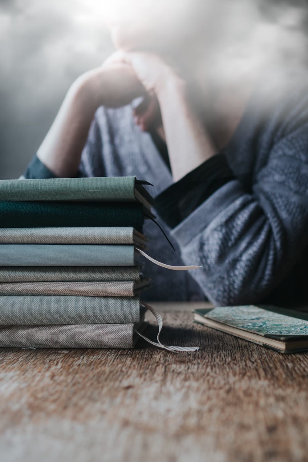 A woman sitting at a table, with a cloud obscuring her face, in front of a pile of notebooks and a small book