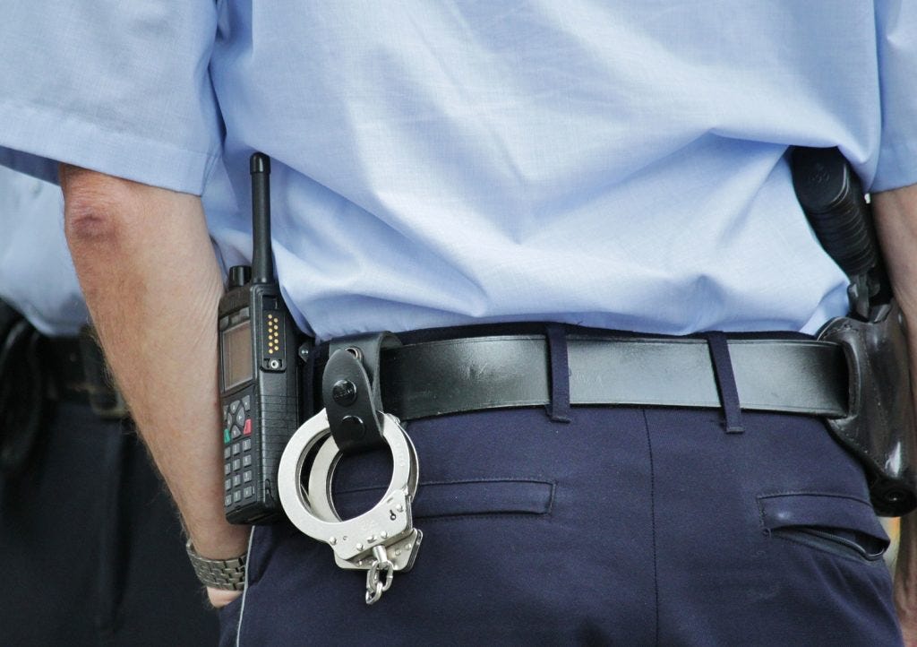 Up close view from the back of two police officers in blue uniforms with handcuffs dangling from one officers belt. Up close view from the back of two police officers in blue uniforms with handcuffs dangling from one officers belt.
