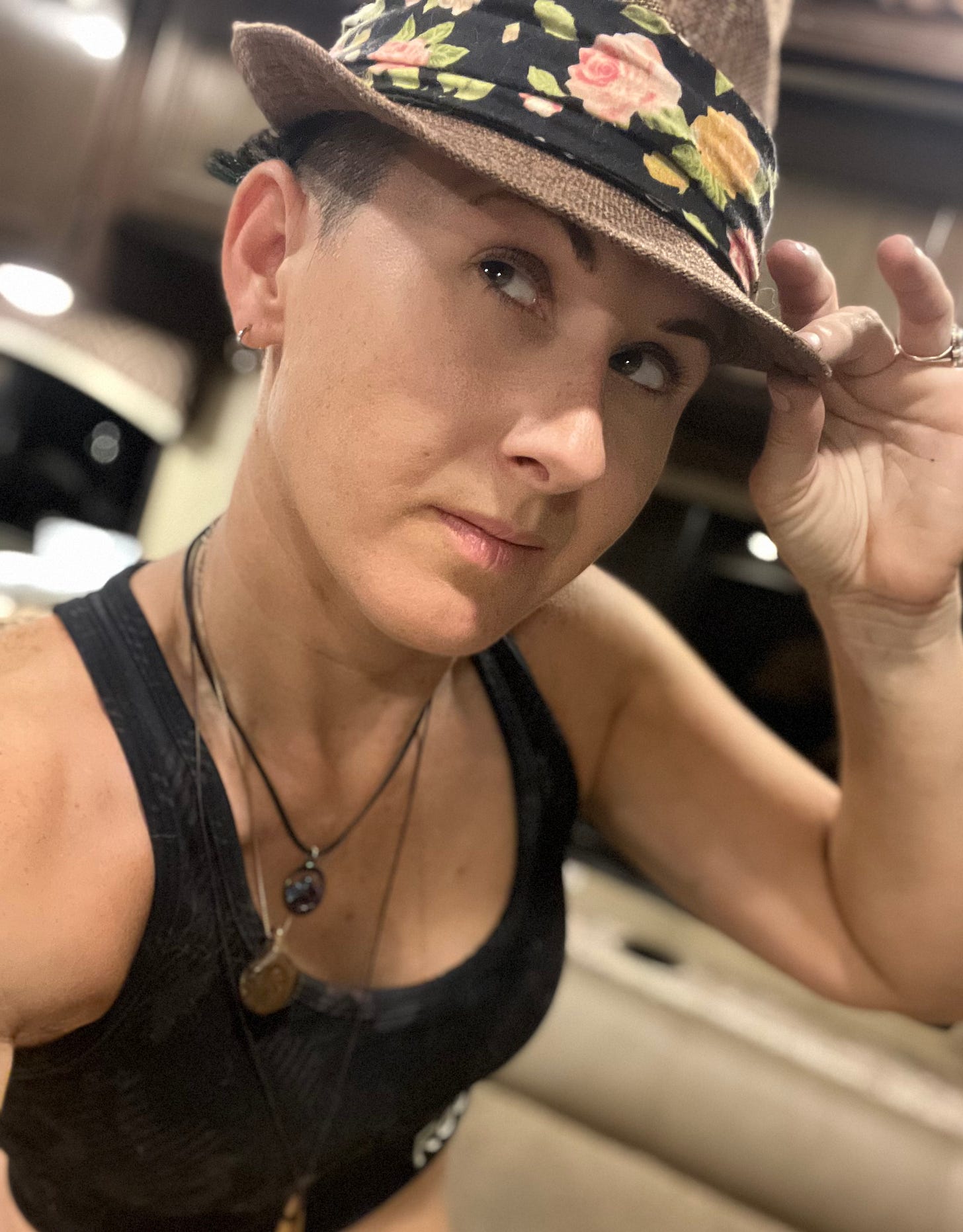 Feeling sharp, Lyric is in a tan fedora hat with a floral print on the hat band. They pose in their RV; one can see it is nighttime as the windows are dark outside. Feeling sharp, Lyric is in a tan fedora hat with a floral print on the hat band. They pose in their RV; one can see it is nighttime as the windows are dark outside.