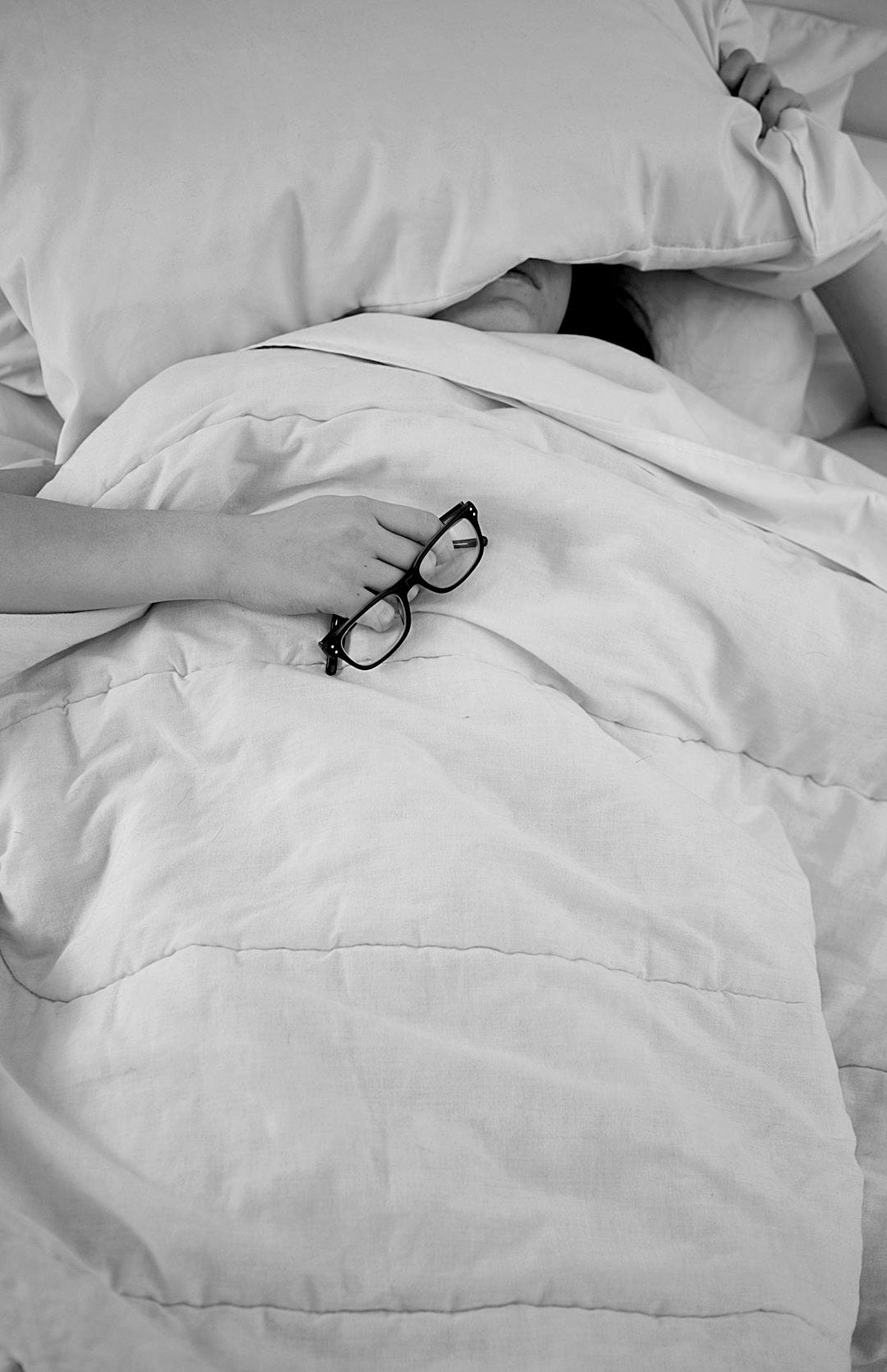 person lying on bed while covering face with pillow and holding eyeglasses person lying on bed while covering face with pillow and holding eyeglasses