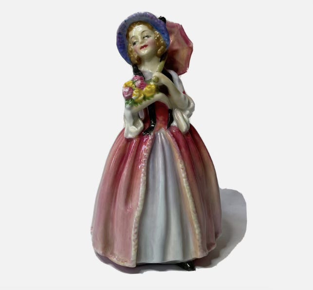 A porcelain figurine of a woman in a pink dress and purple bonnet holding a pink parasol and a bouquet of pink and yellow flowers.