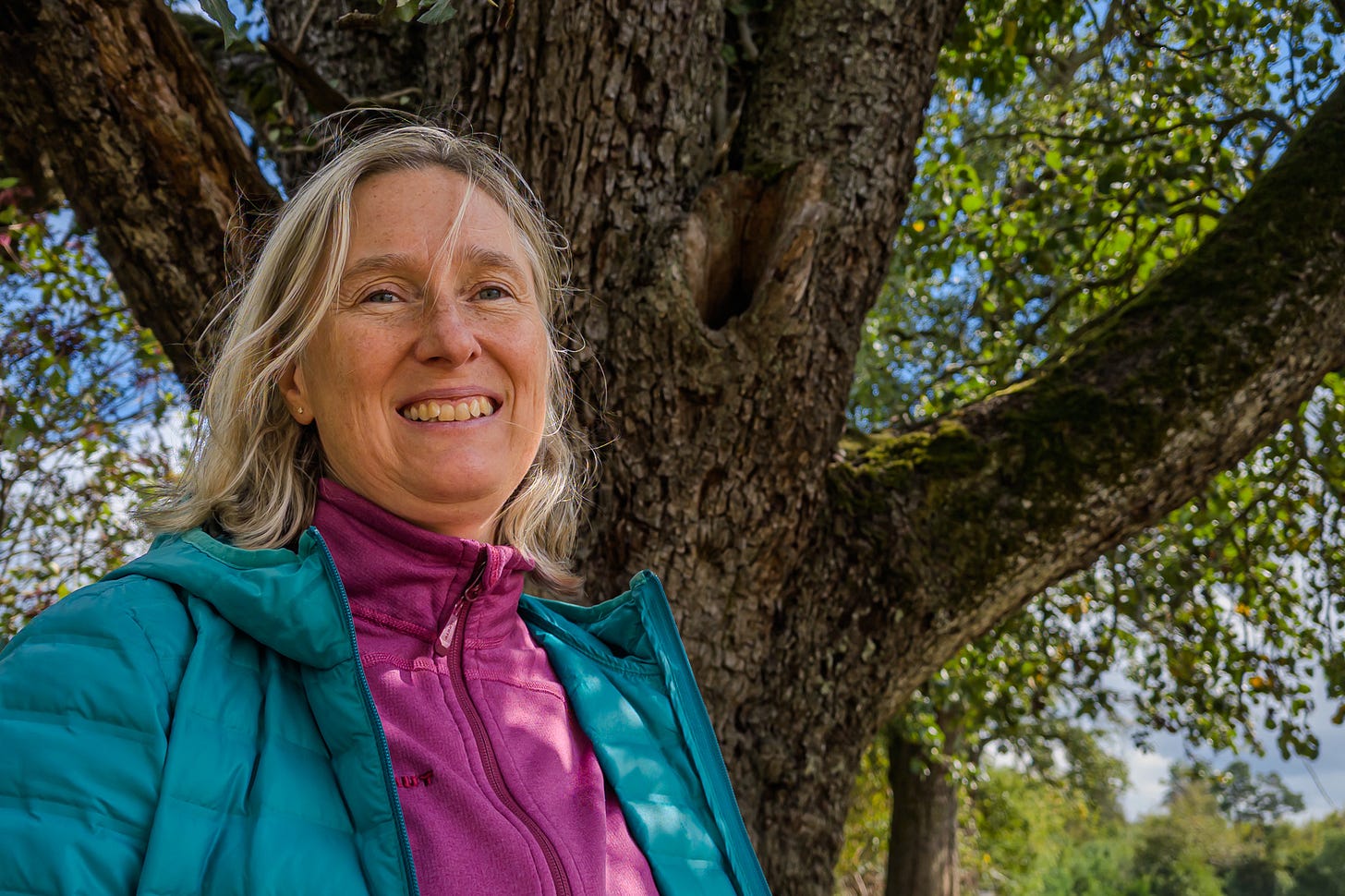 Biodiversitäts-Expertin Véronique Chevillat mit langen blonden Haaren steht vor dem mächtigen, knorrigen Stamm eines alten Birnbaumes. Zwischen den dicken Ästen ist eine natürliche Baumhöhle zu erkennen, die Tieren als Nist- oder Rückzugsort dient. Biodiversitäts-Expertin Véronique Chevillat mit langen blonden Haaren steht vor dem mächtigen, knorrigen Stamm eines alten Birnbaumes. Zwischen den dicken Ästen ist eine natürliche Baumhöhle zu erkennen, die Tieren als Nist- oder Rückzugsort dient.