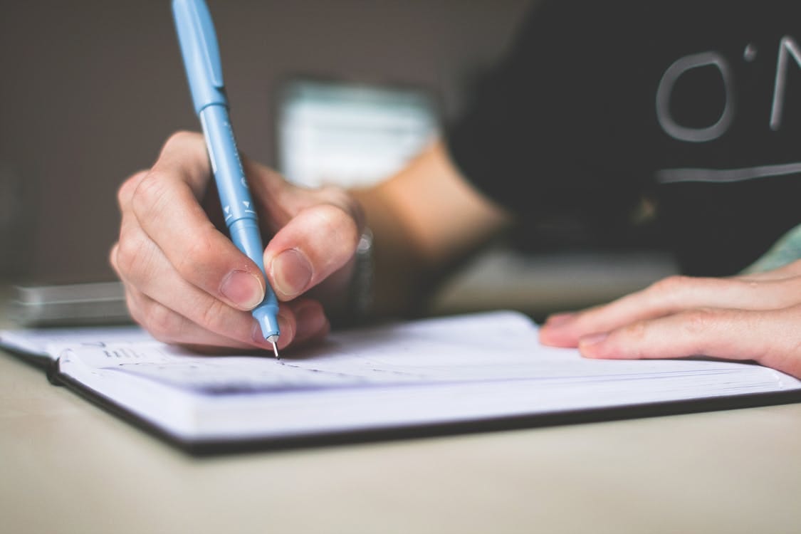 A close-up of a hand holding a blue pen, writing in a notebook