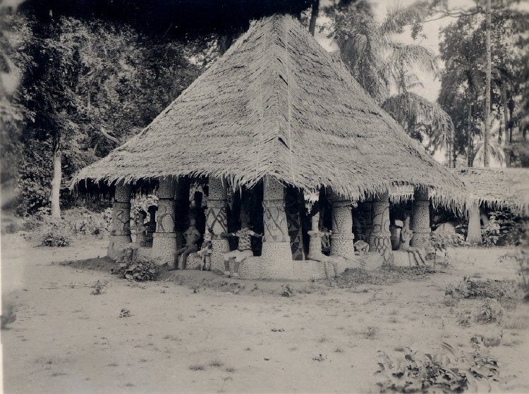A square thatched building with decorative columns, 4 per side, with full clay figures seated around the edges. Sepia toned photo